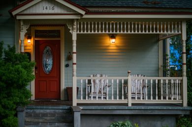 The front porch of a house with a red door and a white railing.