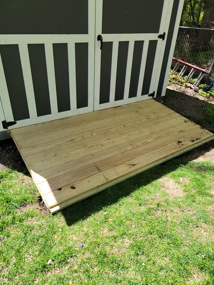 A wooden deck is sitting in the grass next to a shed.