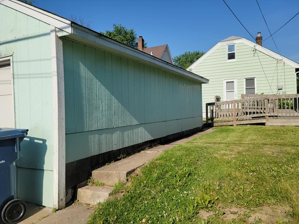 A green house with a blue trash can in front of it.