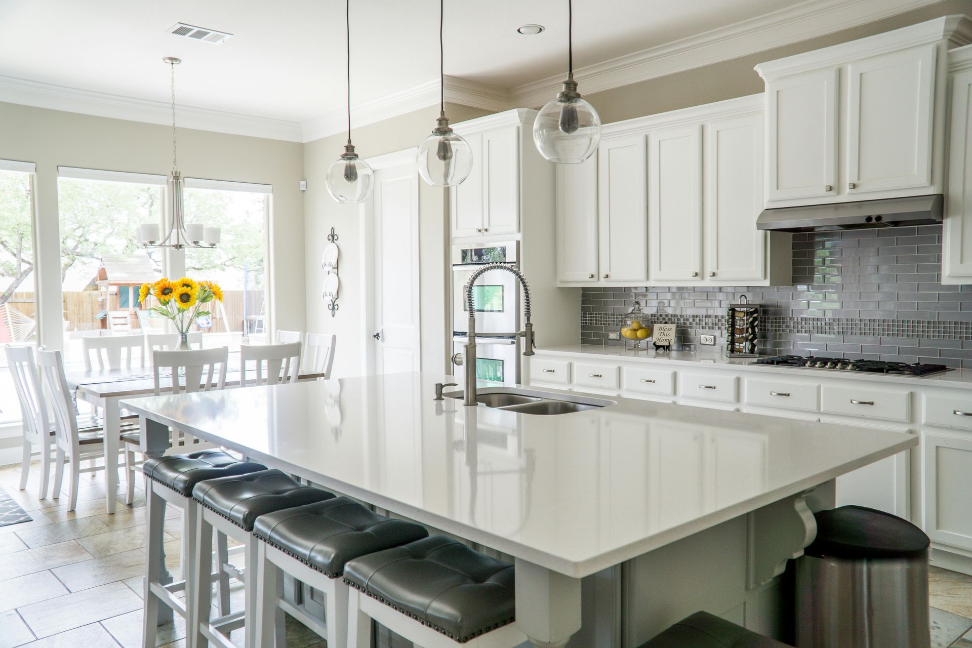 Bright white kitchen with island seating, pendant lights, and dining area by large windows