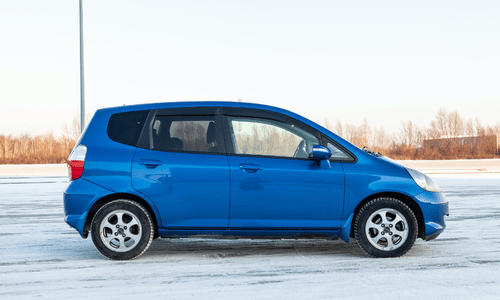 Blue Honda Fit parked on a snowy roadside under a pale sky