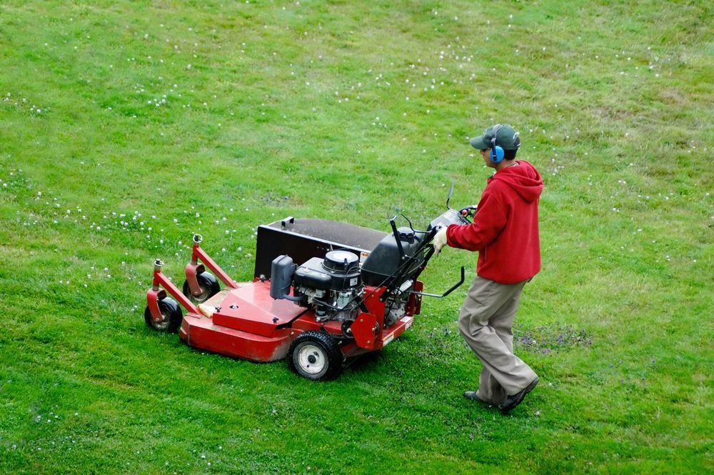 Person Mowing Grass with A Red Zero-Turn Mower; Wearing Red Jacket and Hearing Protection on A Green Lawn — Young's Lawn Care In Glenden, QLD