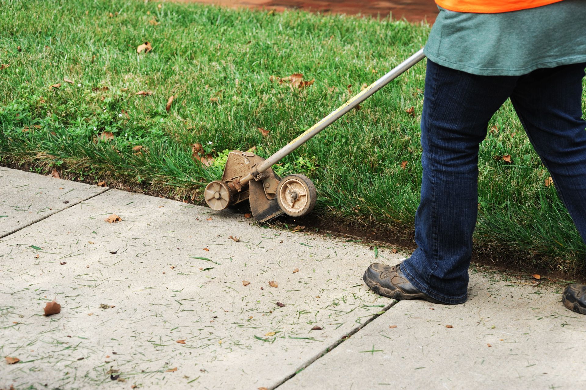Person Edging Grass Alongside a Sidewalk with A Wheeled Trimmer — Young's Lawn Care In Glenden, QLD