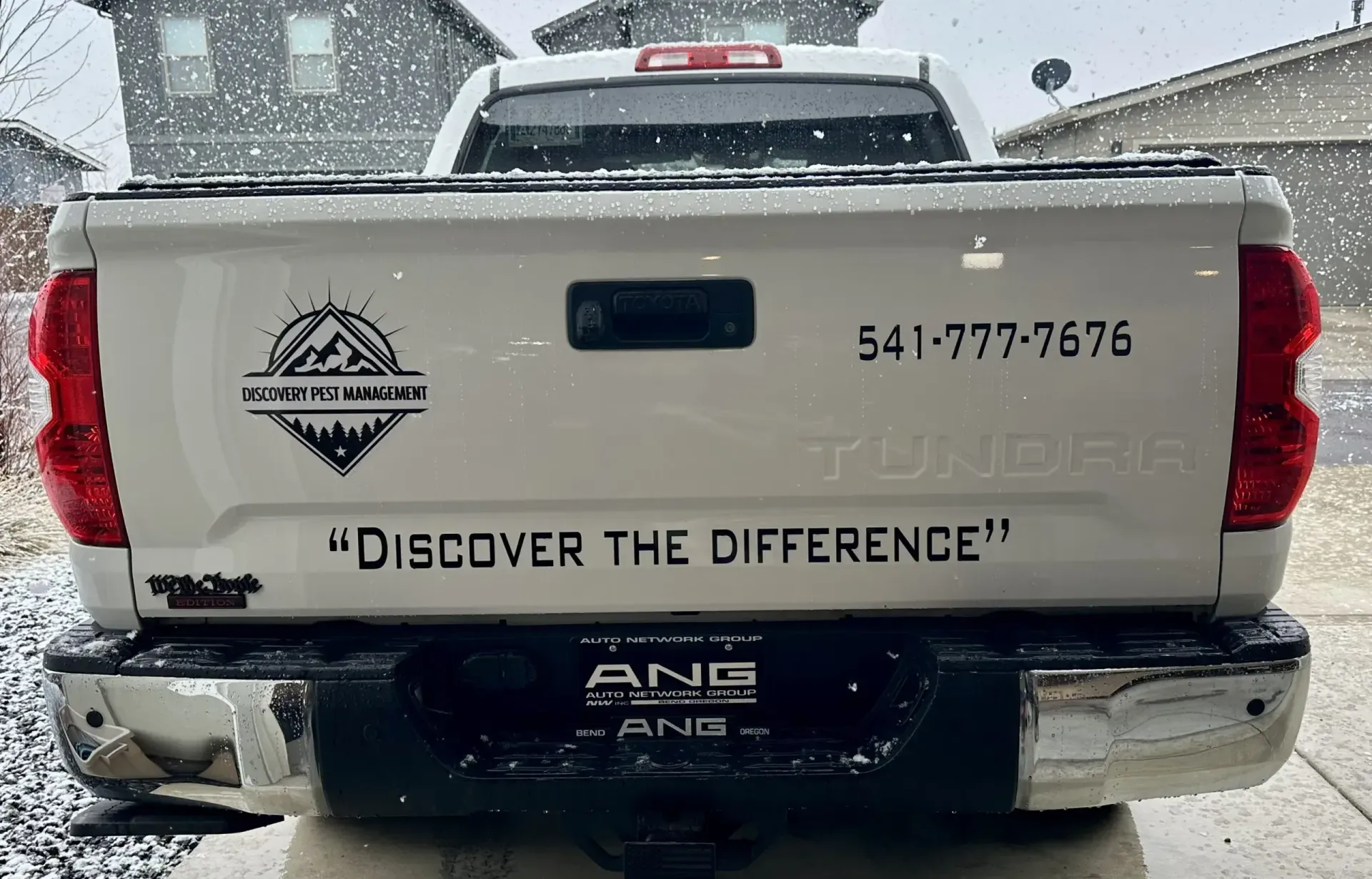 White Toyota Tundra pickup truck's rear, snowy scene. The truck has a logo and phone number on the tailgate and bumper.