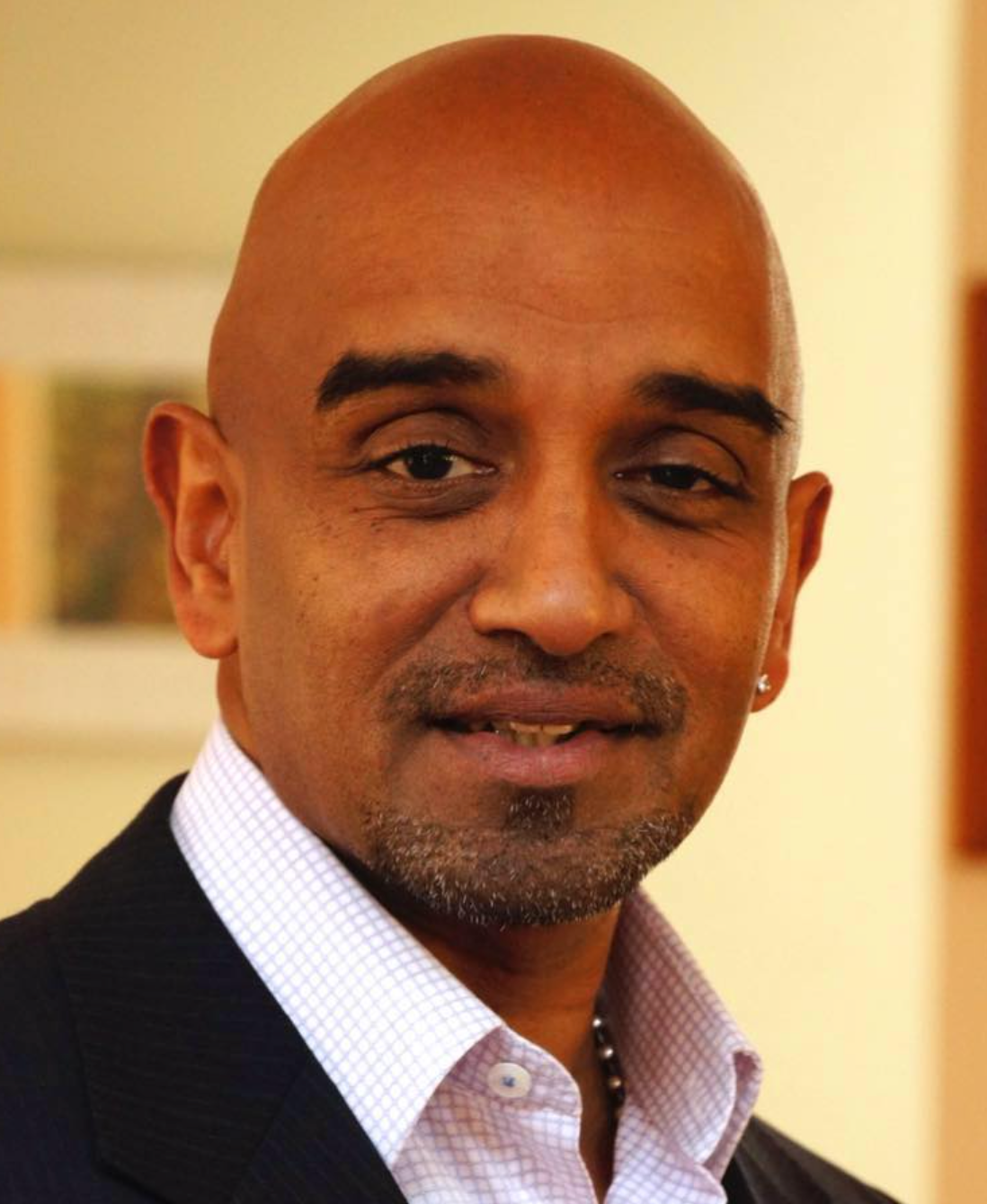 Bald man with a goatee wearing a suit jacket and collared shirt smiles, indoors.