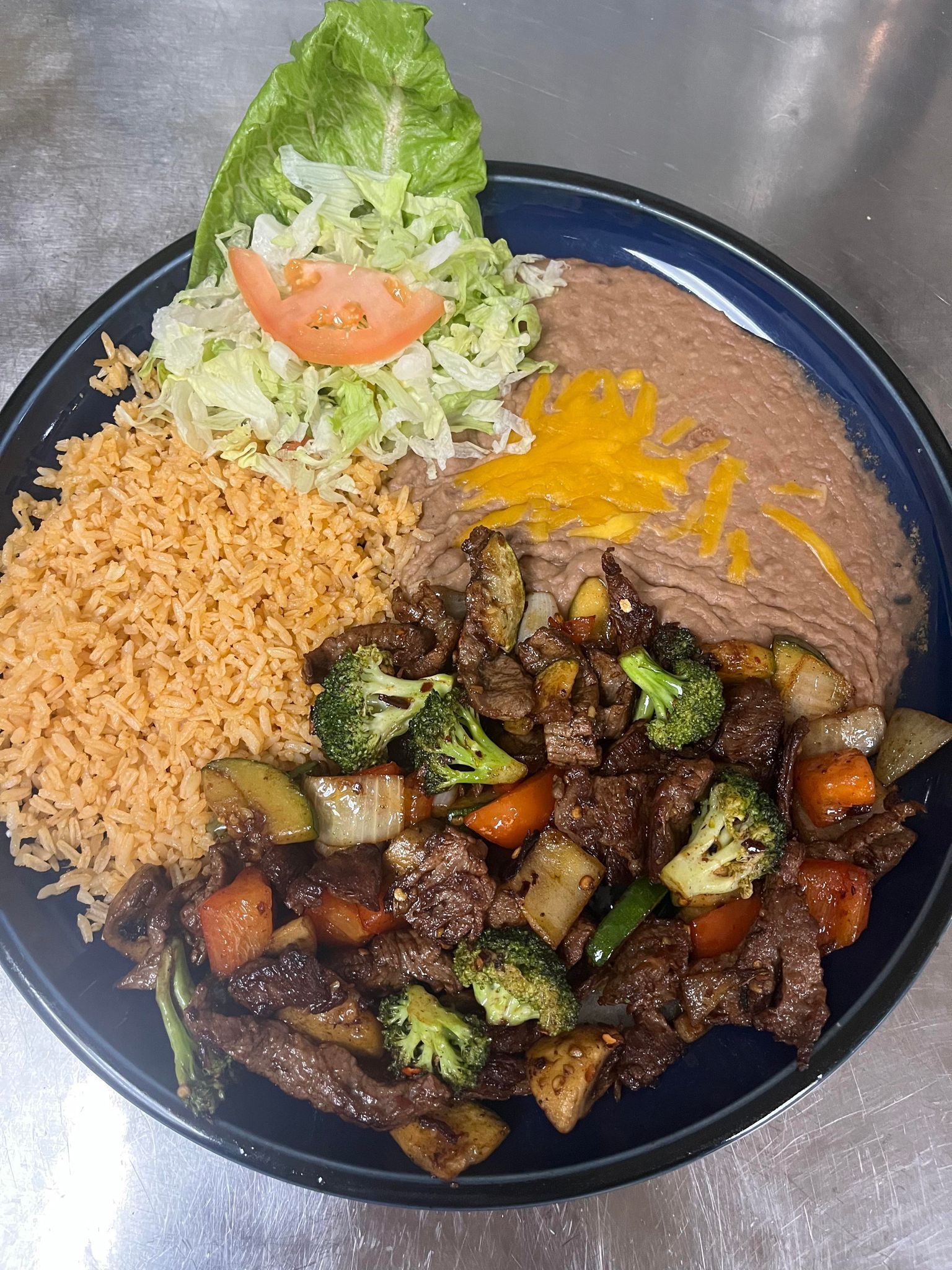 A plate of steak with rice , beans , broccoli and tomatoes on a table.