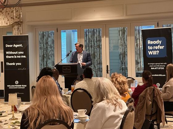 A man speaking at a podium at a conference. Audience sits at tables. Banners flank the stage.