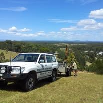 White SUV with trailer parked on a hill overlooking a green landscape on a sunny day. A person is near the trailer — Rosewood Environmental Services Pty Ltd in Wauchope, NSW