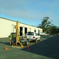 Drilling rig with a white SUV parked near a commercial building — Rosewood Environmental Services Pty Ltd in Wauchope, NSW
