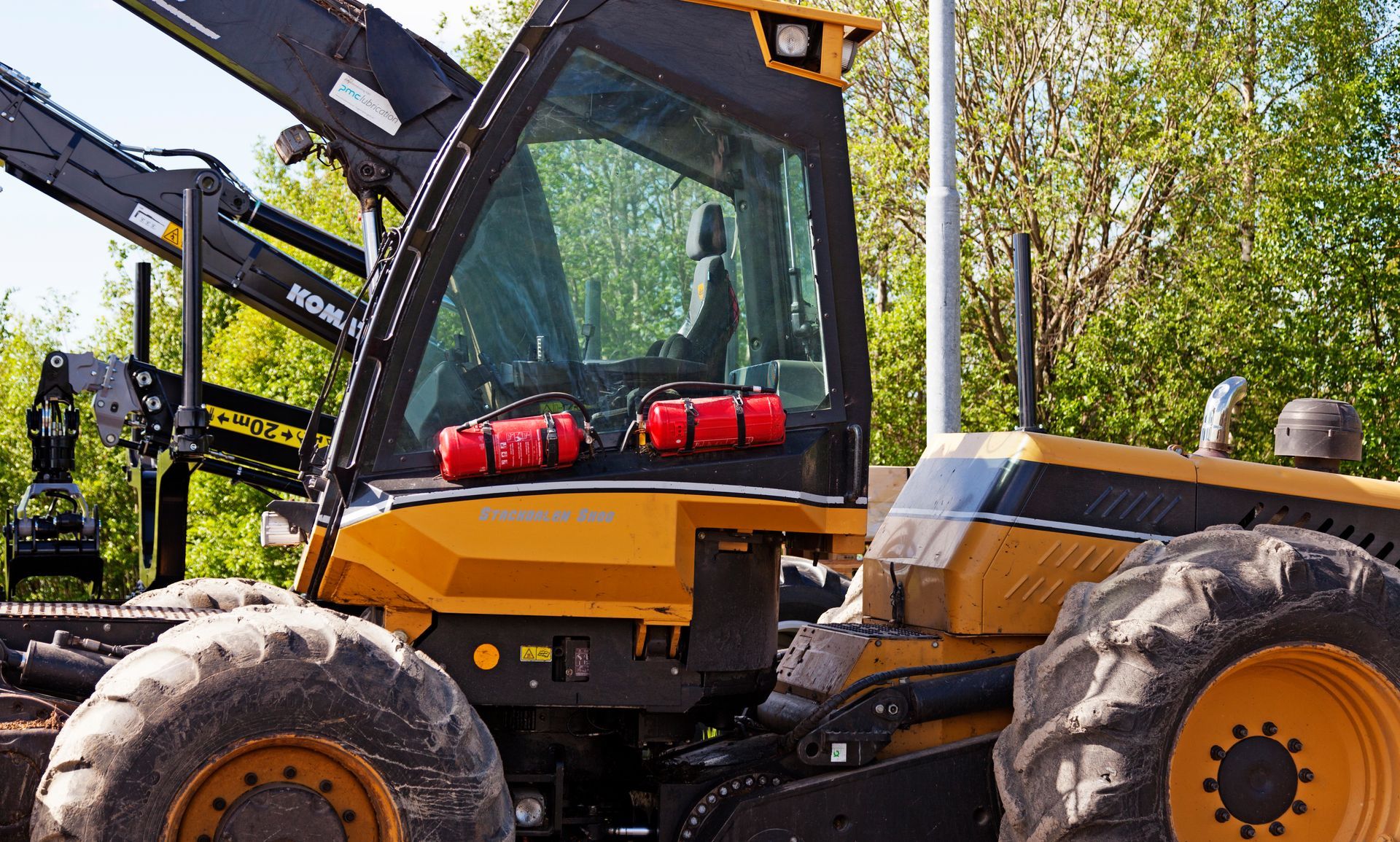 Yellow forestry machine with large tires and a glass-enclosed cab; red tool kits sit inside.
