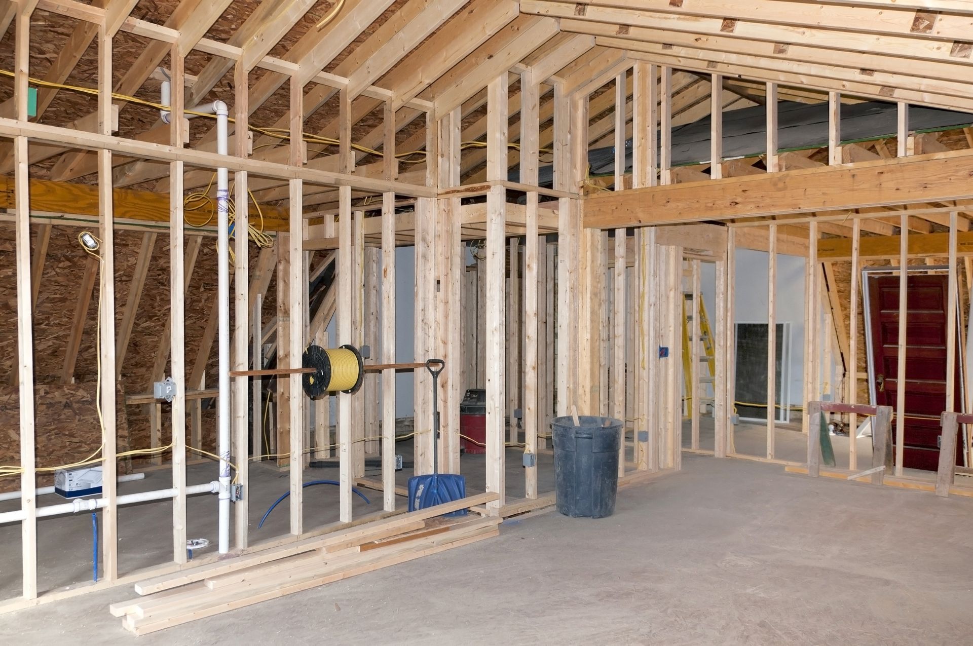 Interior of a building under construction. Wood framing with concrete floor; electrical wiring and plumbing visible.