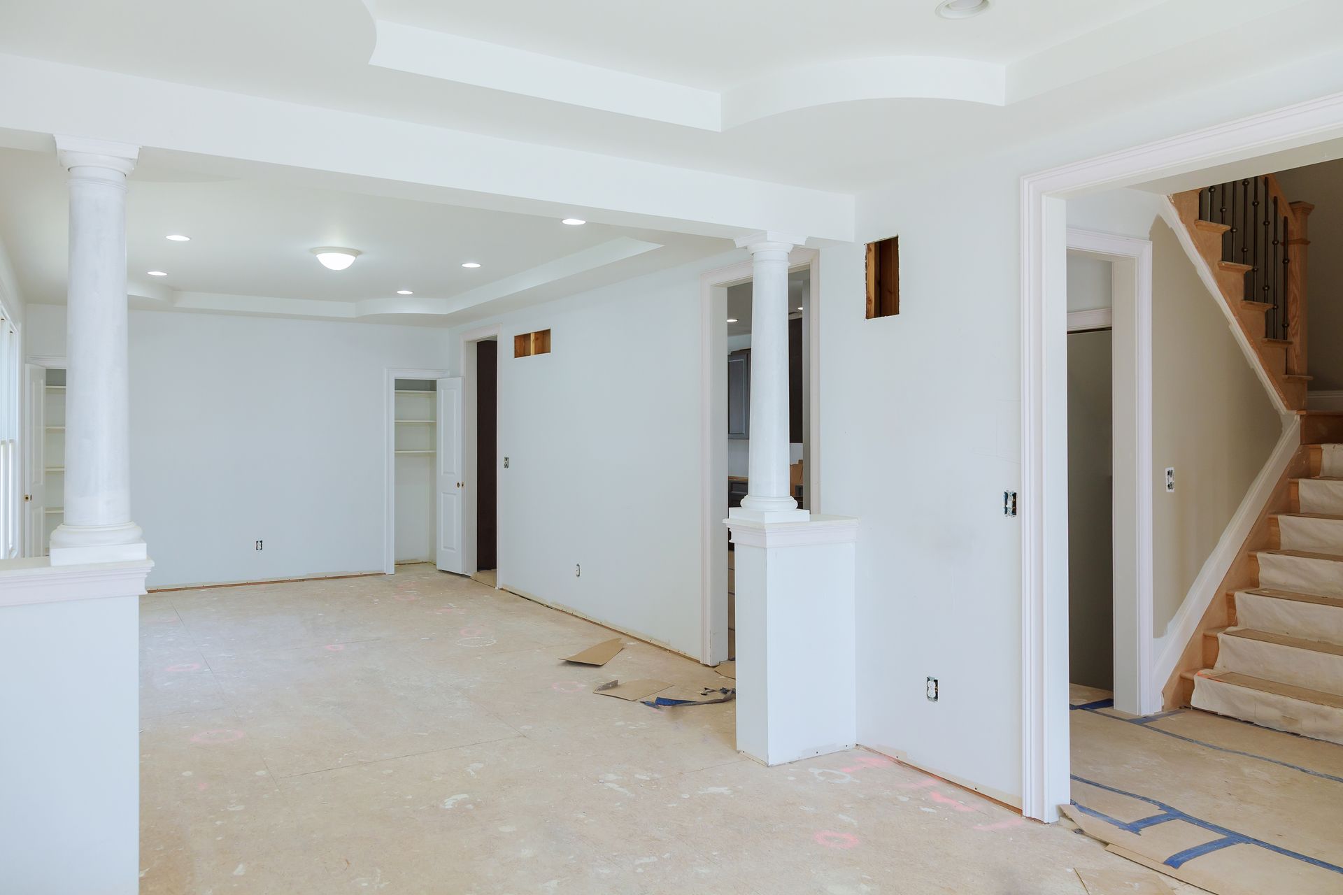 Interior of a house under construction; white walls, pillars, and a staircase.
