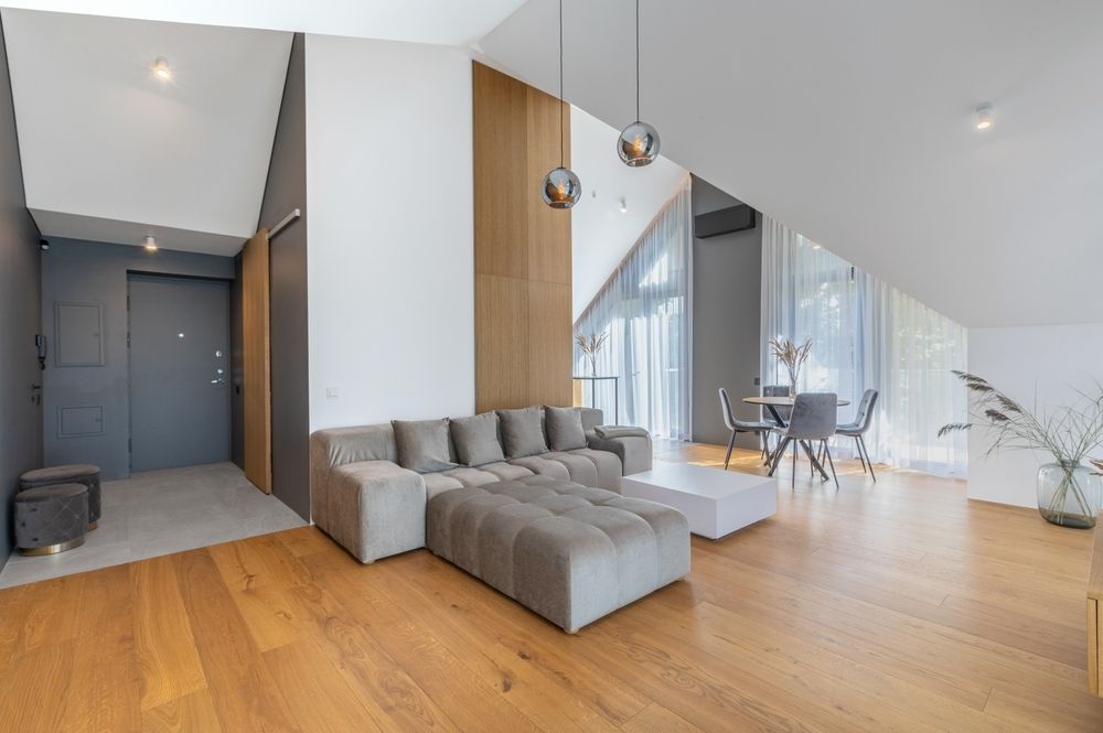 Modern living room with light wooden floors, gray sofa, and dining area.