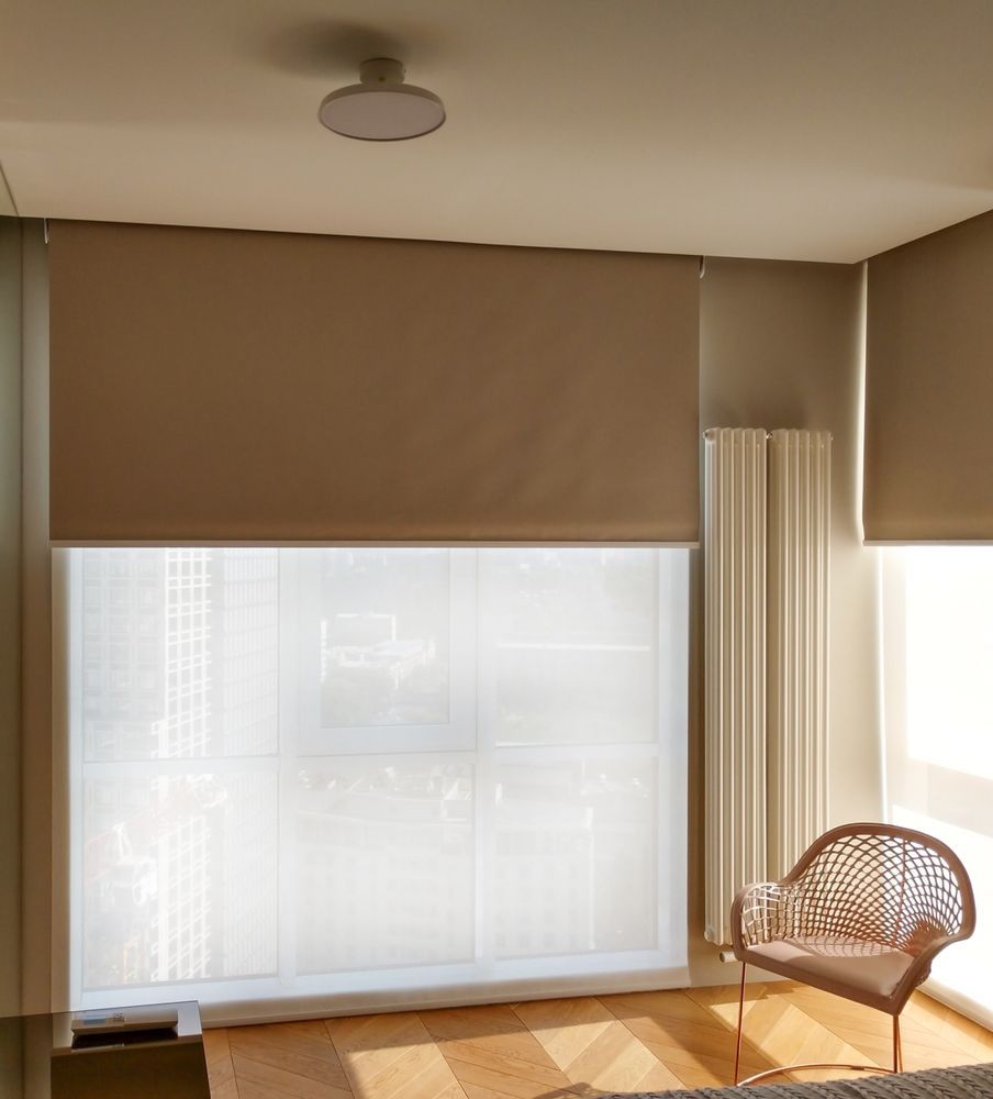Room with beige and white roller shades, a radiator, and a chair.