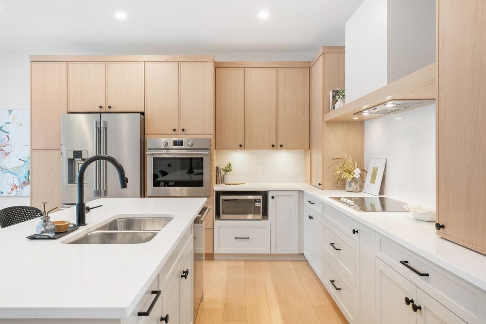 Modern kitchen with light wood and white cabinets, stainless steel appliances, and a black faucet.