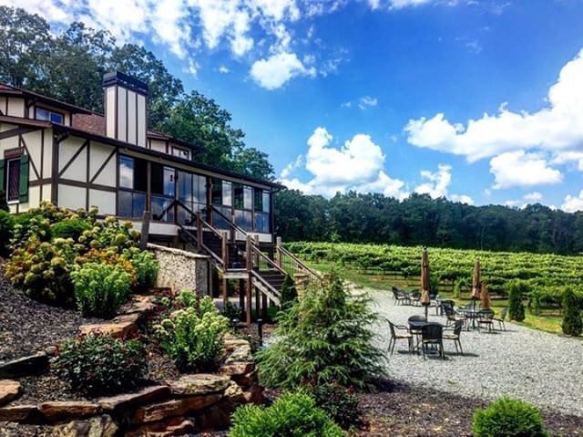 A large house in the middle of a vineyard with tables and chairs in front of it.