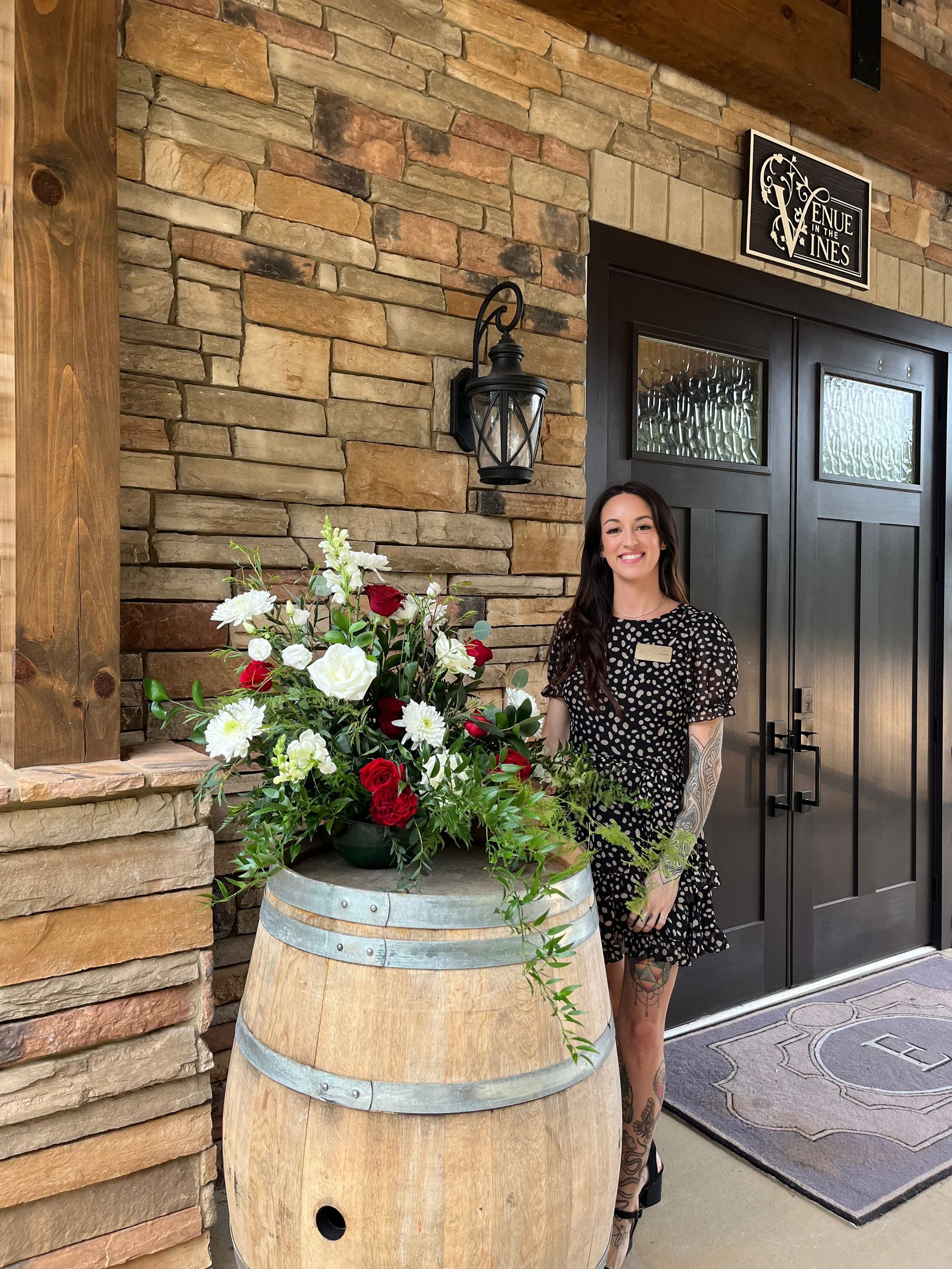 A woman is standing next to a wooden barrel with flowers on it.