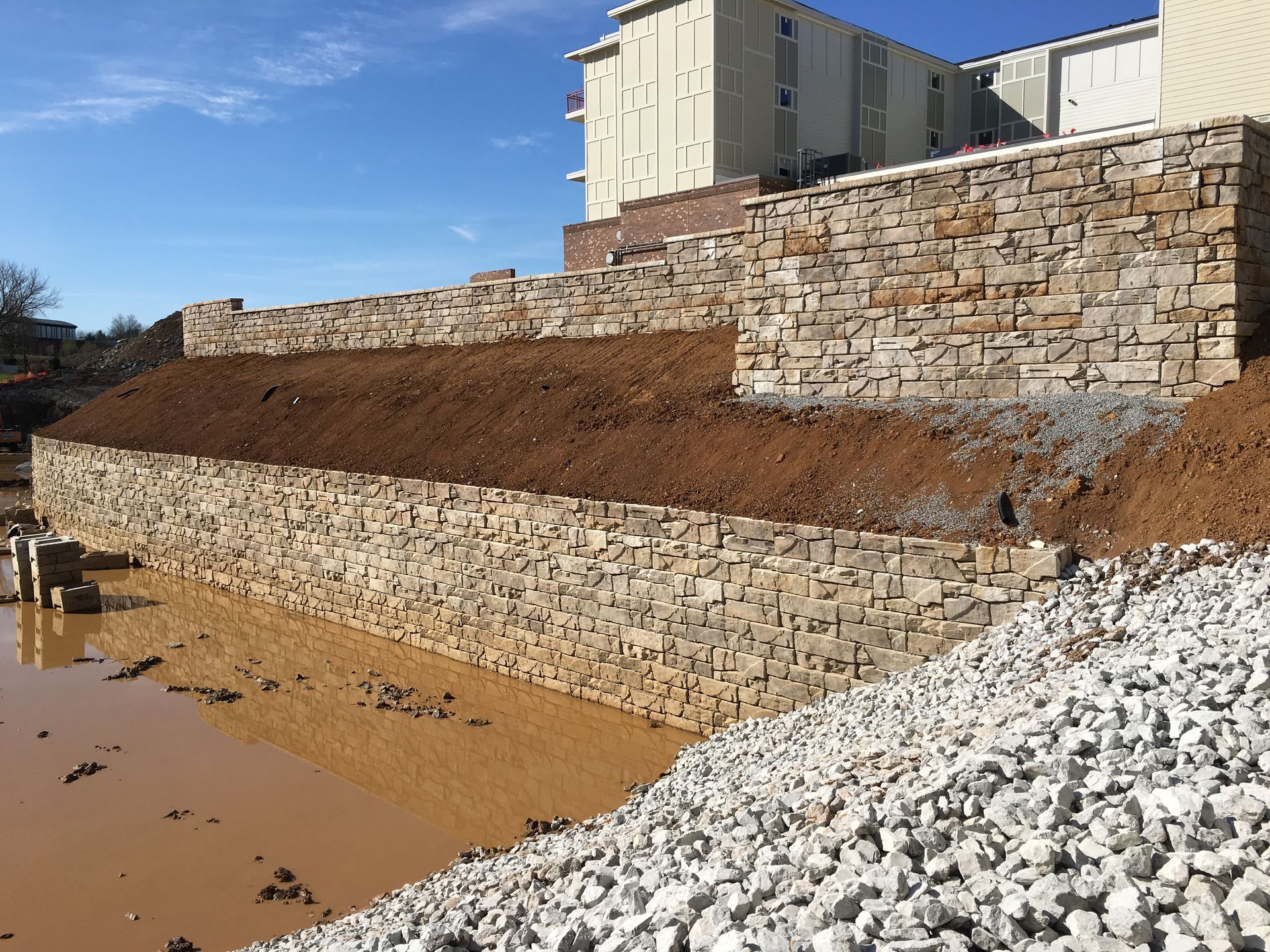A large stone wall is sitting on top of a hill next to a pile of gravel.