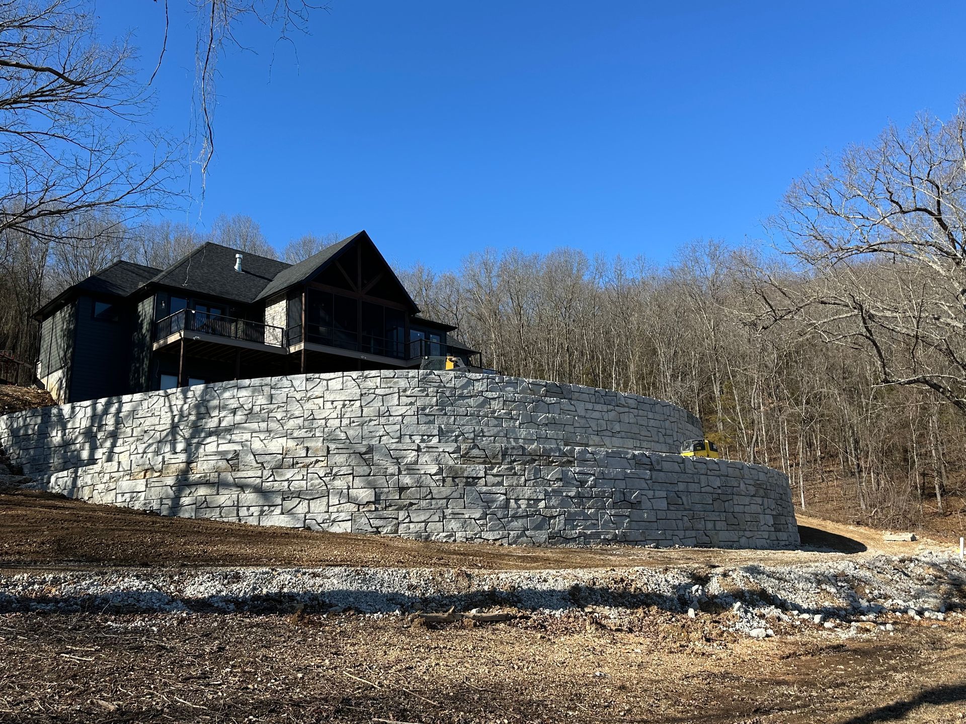 A large house is sitting on top of a hill next to a large stone wall.
