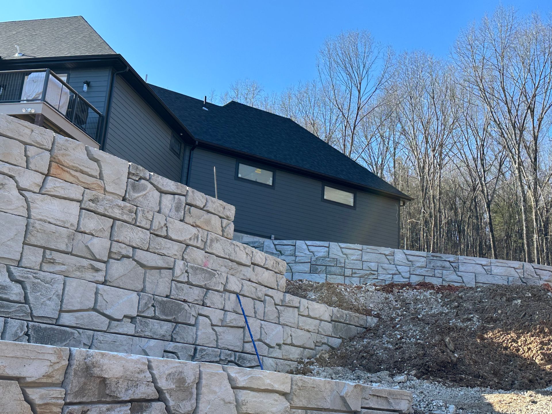 A large house is sitting on top of a hill next to a stone wall.