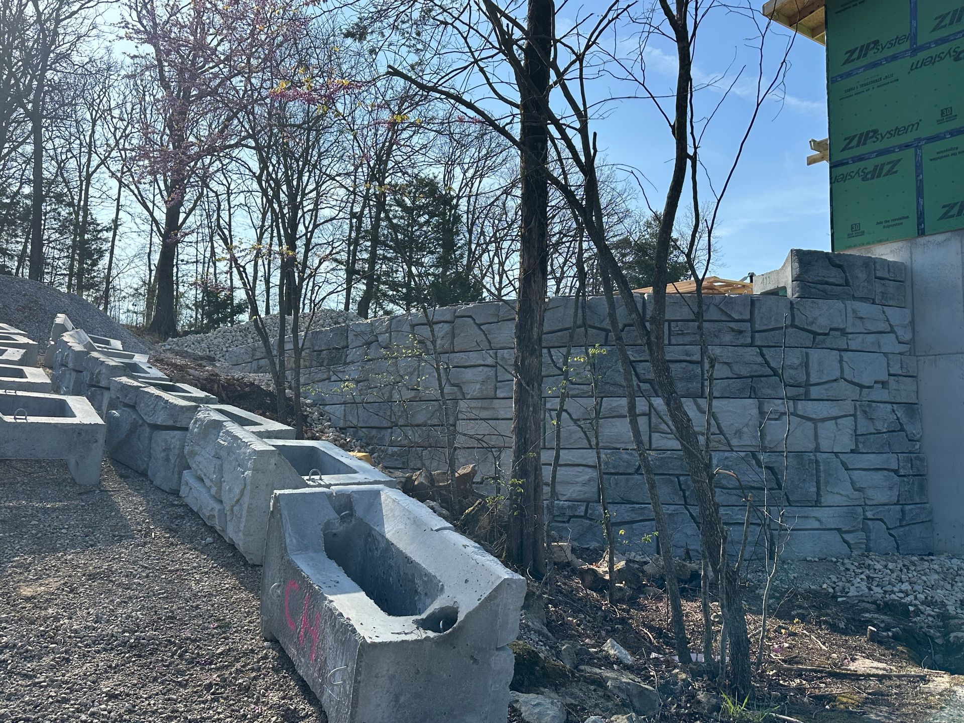 A stone wall is being built on a hill with trees in the background.