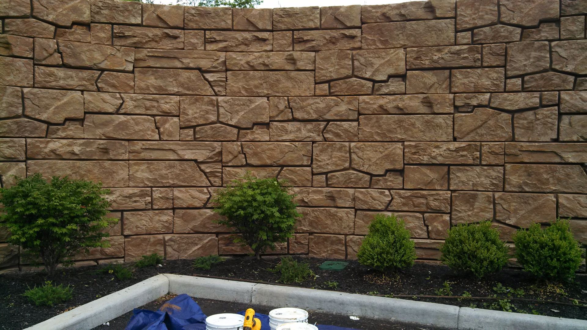 A brick wall with a blue tarp on the ground in front of it