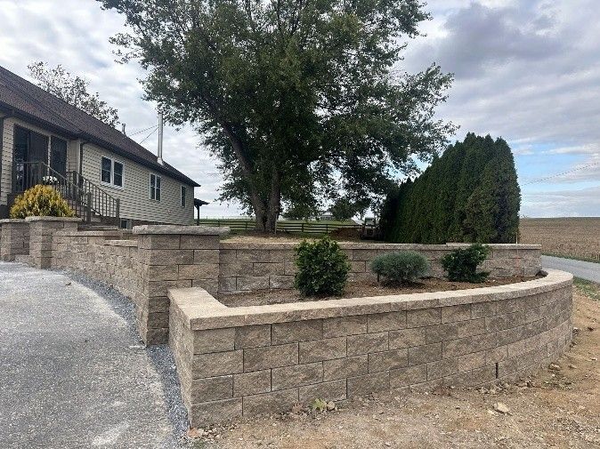 Curved tiered concrete block retaining wall with shrubs beside a home and driveway