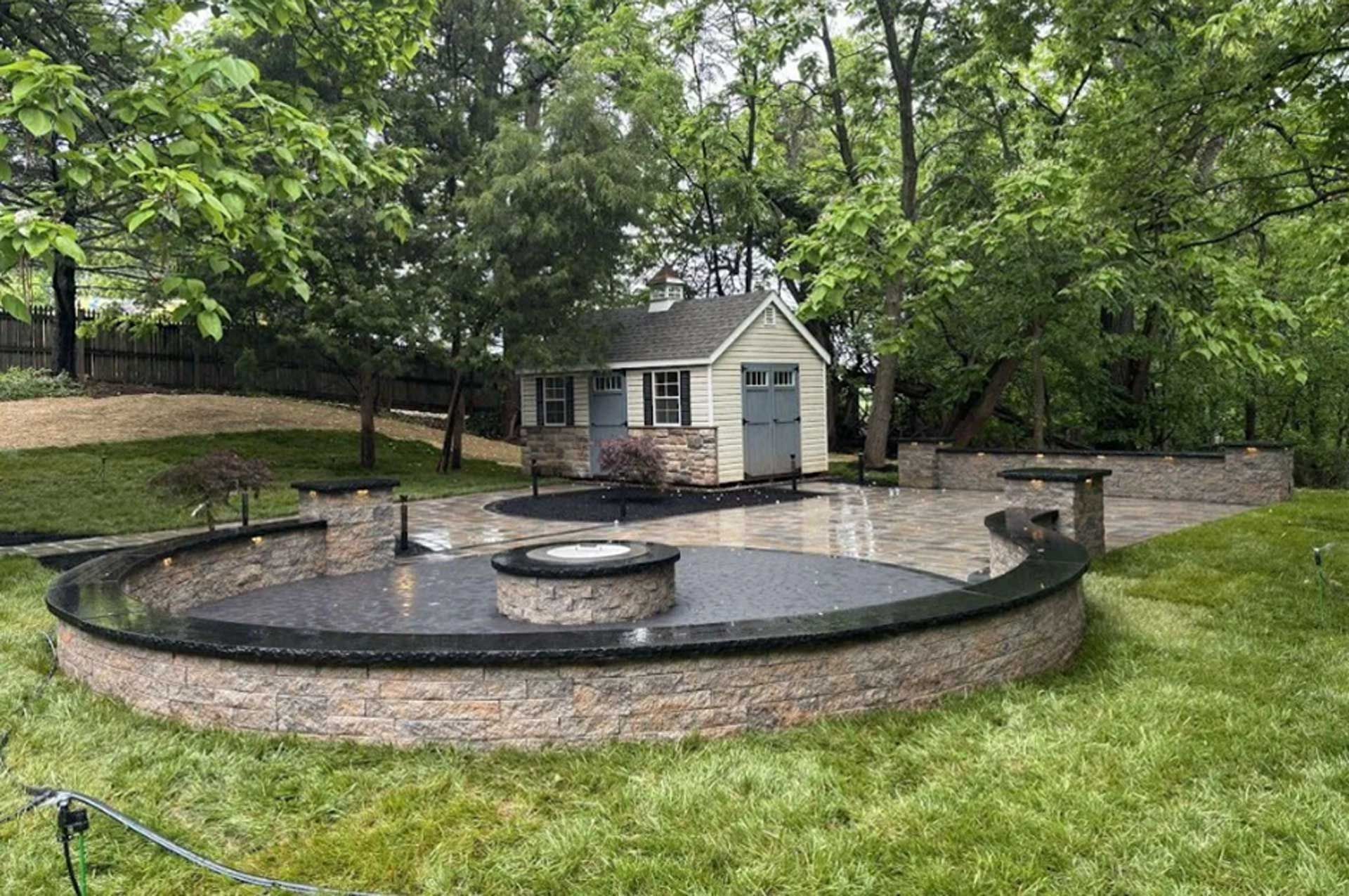 Stone patio with retaining wall and steps in a backyard.