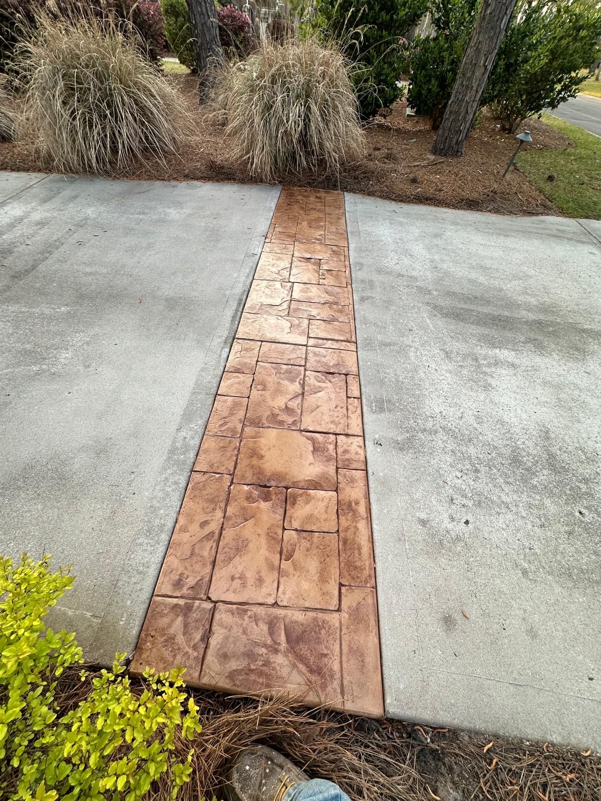A concrete walkway leading to a driveway with a brick pattern.