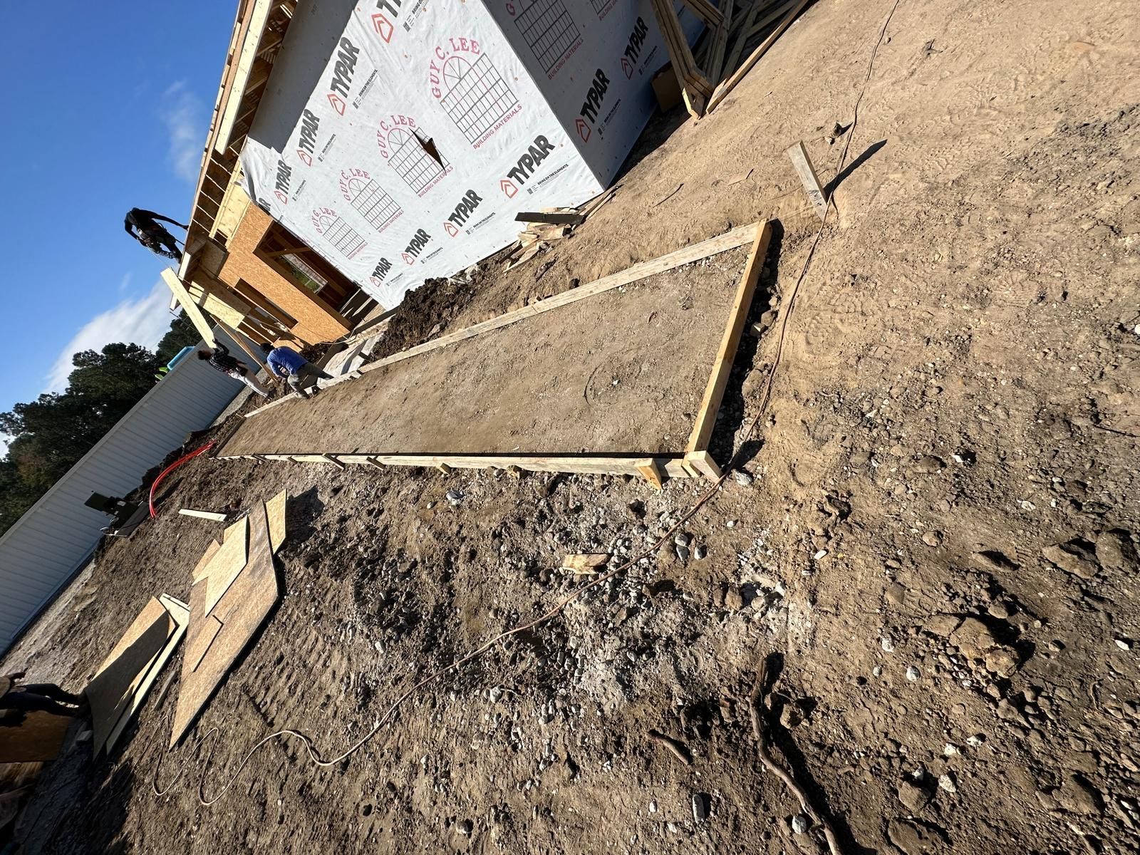 A concrete walkway is being built in front of a house under construction.