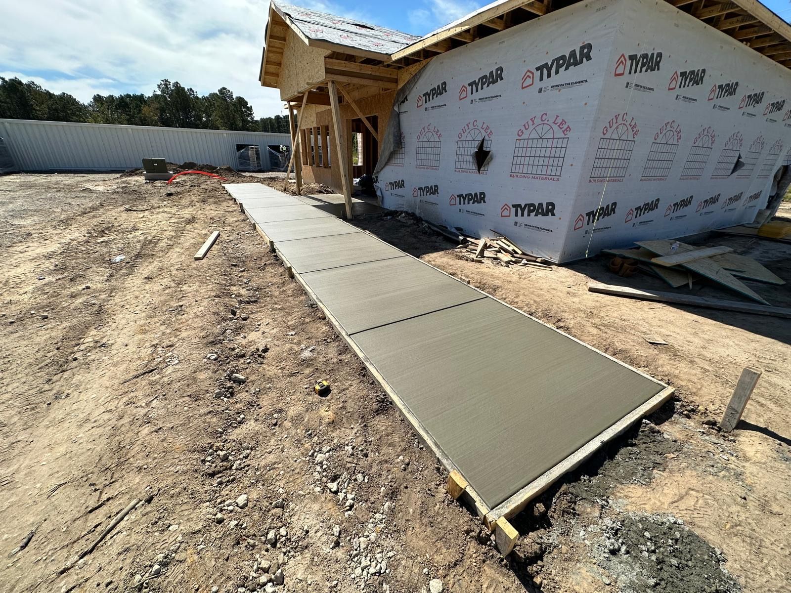 A concrete walkway is being built in front of a house under construction.