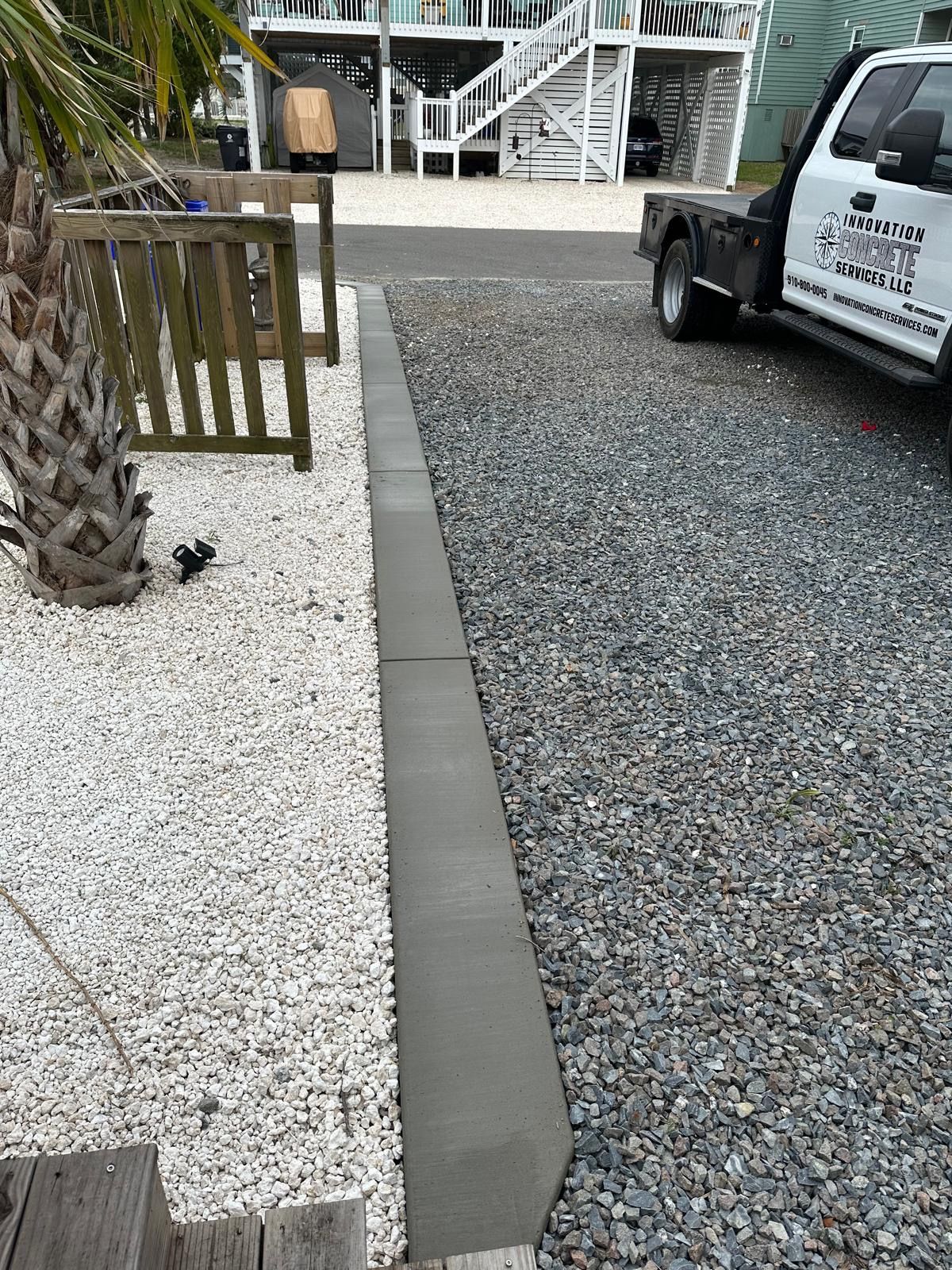 A tow truck is parked in a gravel driveway next to a palm tree.