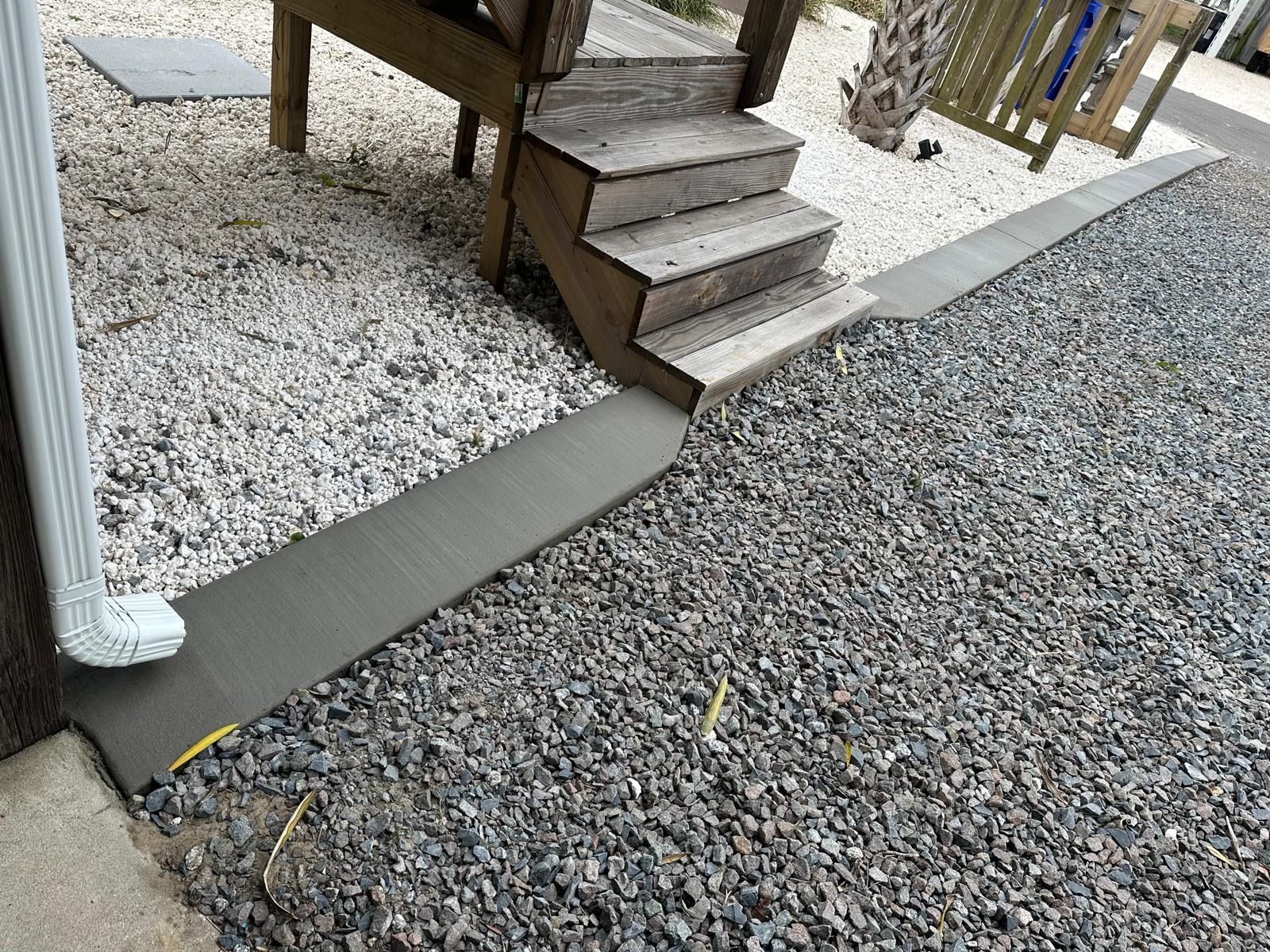 A gravel driveway with a wooden deck and stairs.