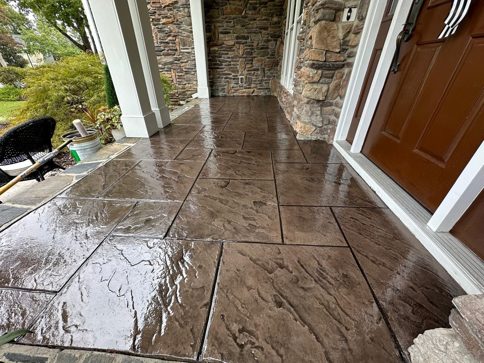 A concrete porch with a stone wall and a brown door.