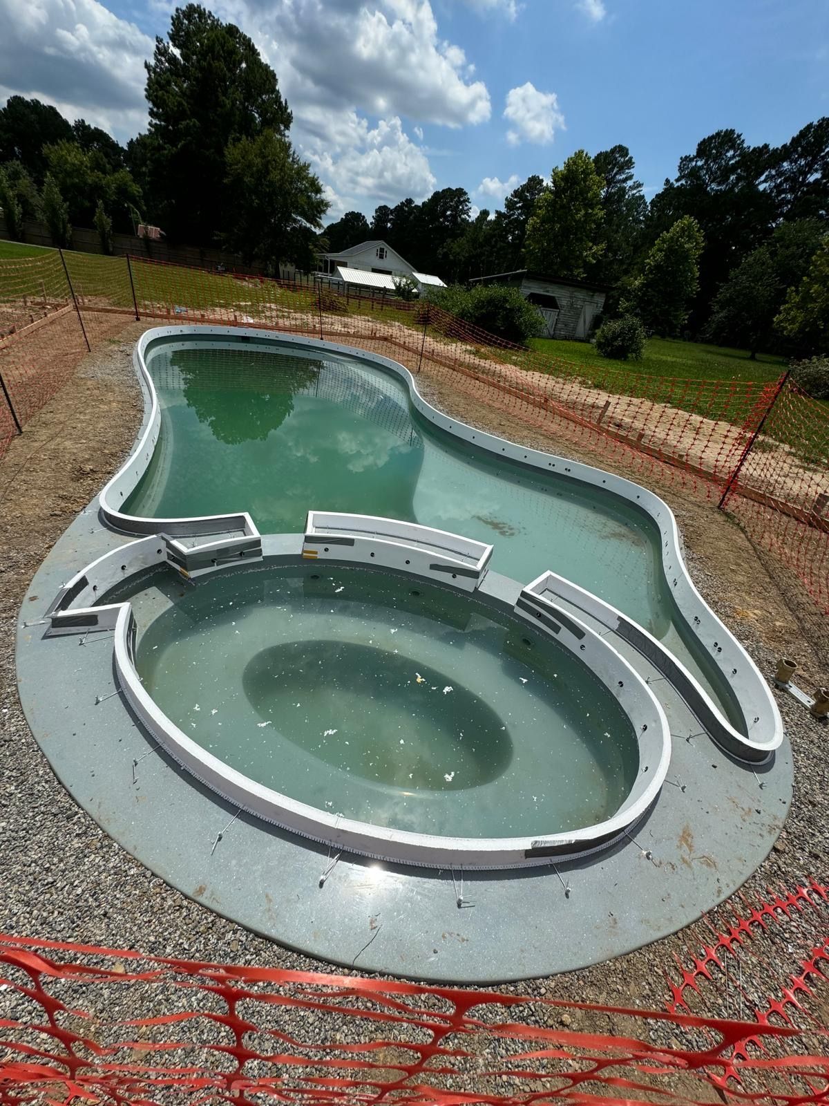 A large swimming pool is surrounded by gravel and a fence.