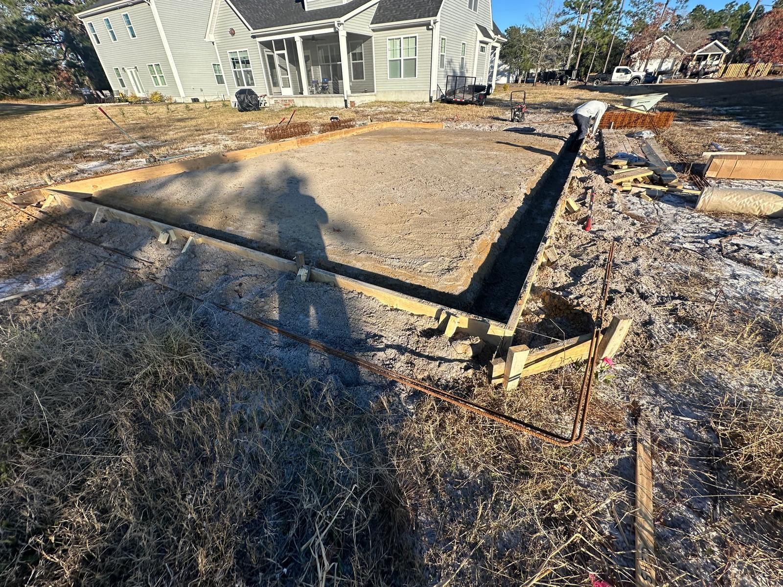 A man is working on a concrete foundation in front of a house.