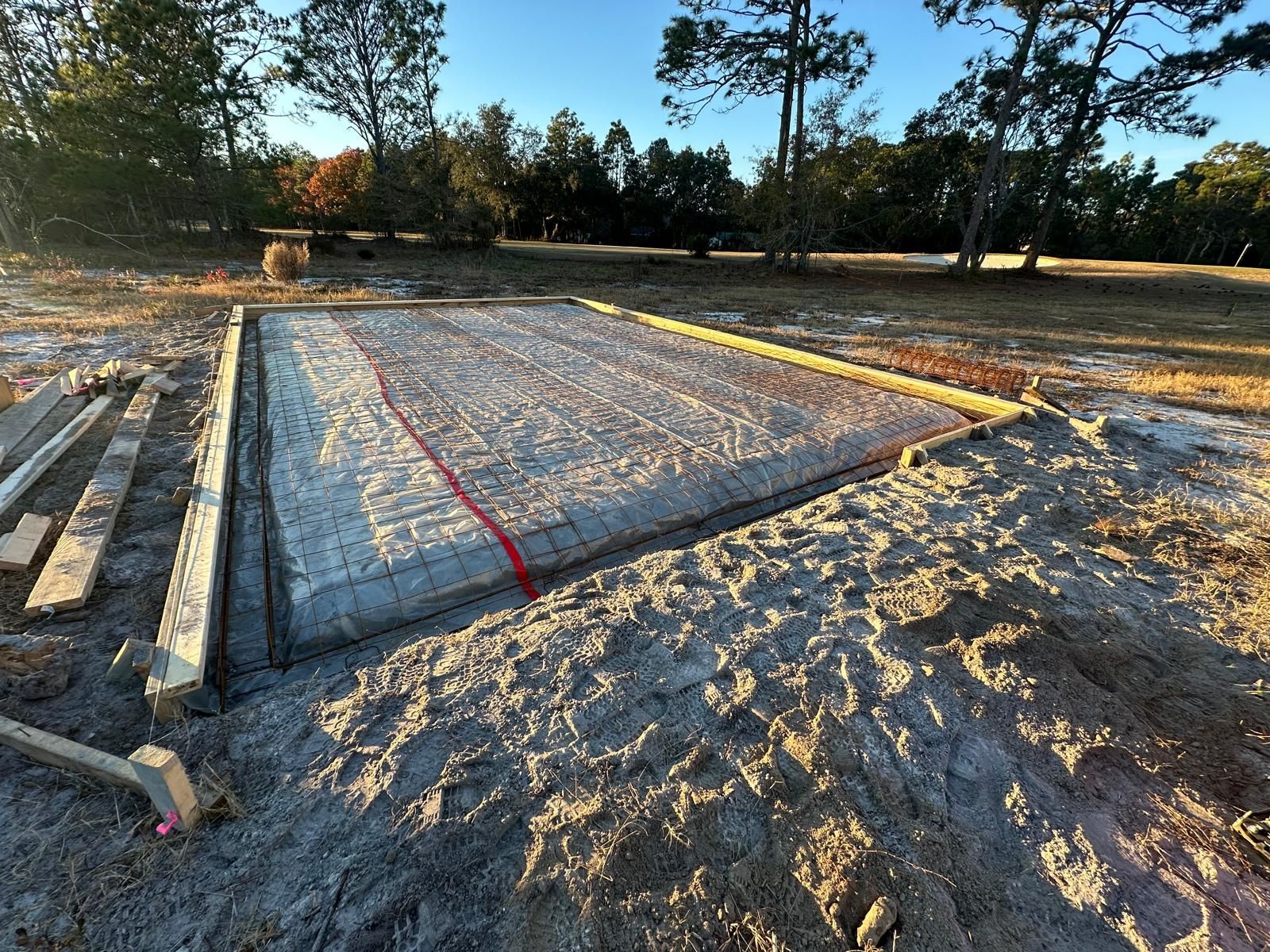 A concrete base is being built in a dirt field with trees in the background.