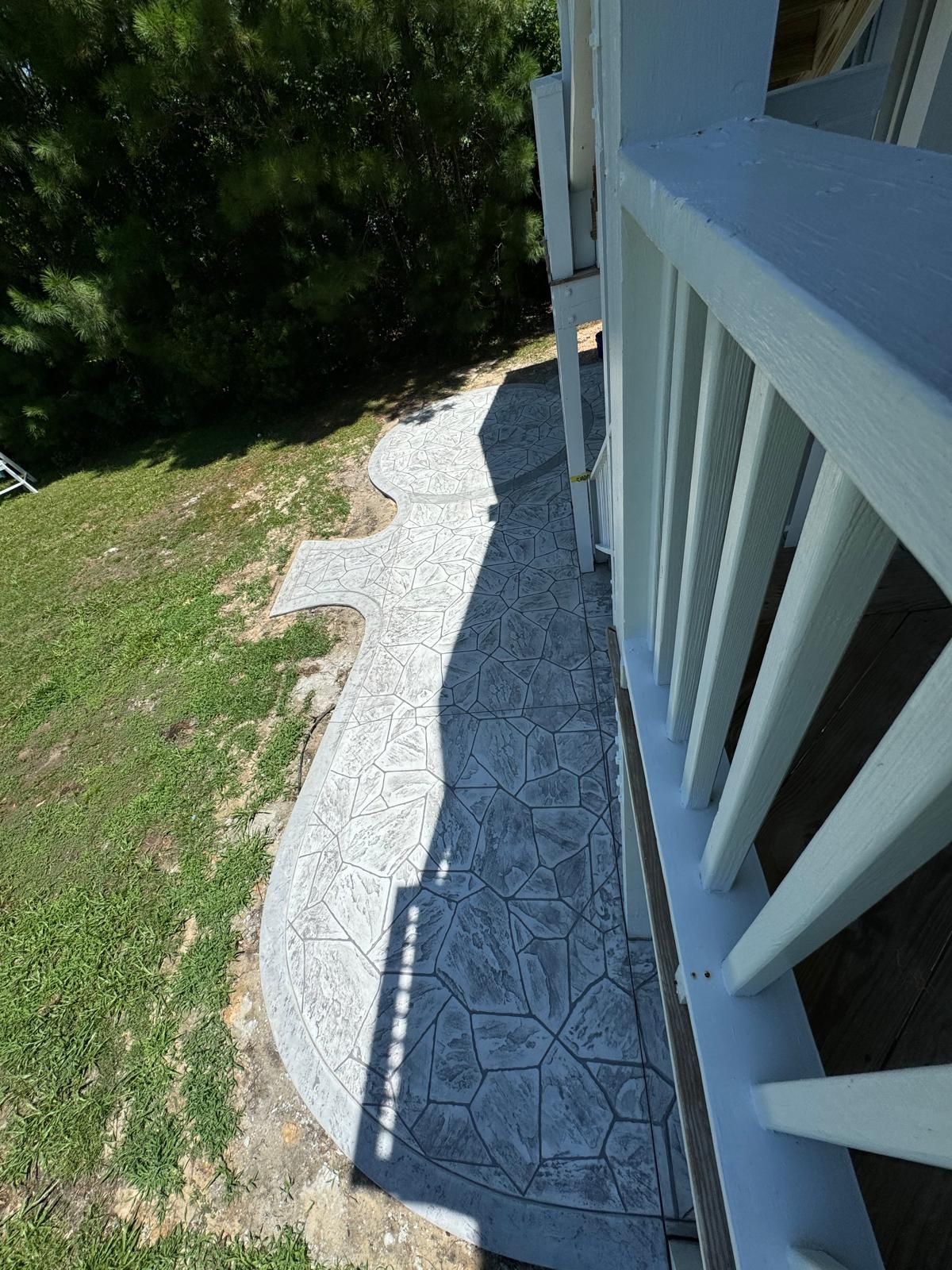 A concrete walkway leading to a white railing on the side of a house.