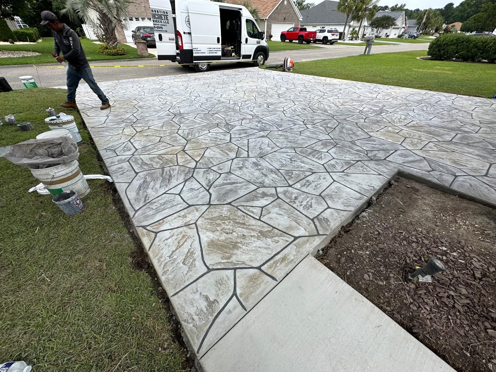A man is working on a concrete driveway next to a van.