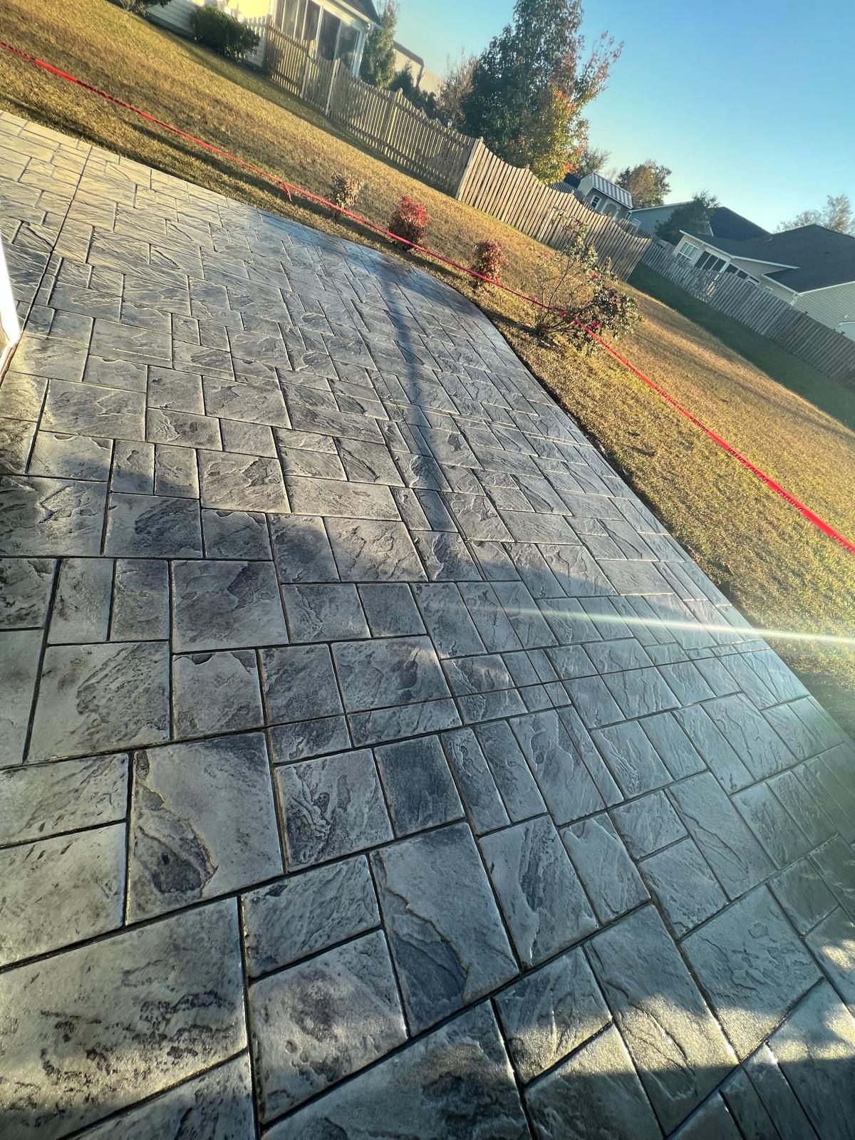 A concrete walkway with a brick pattern is being installed in a backyard.