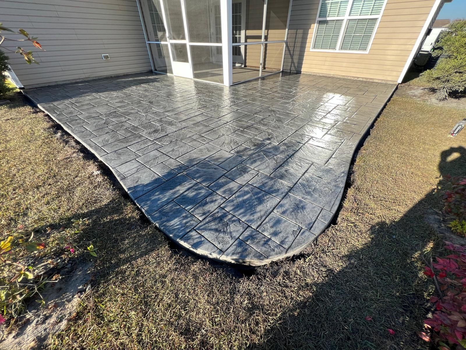 A concrete patio in front of a house with a screened in porch.
