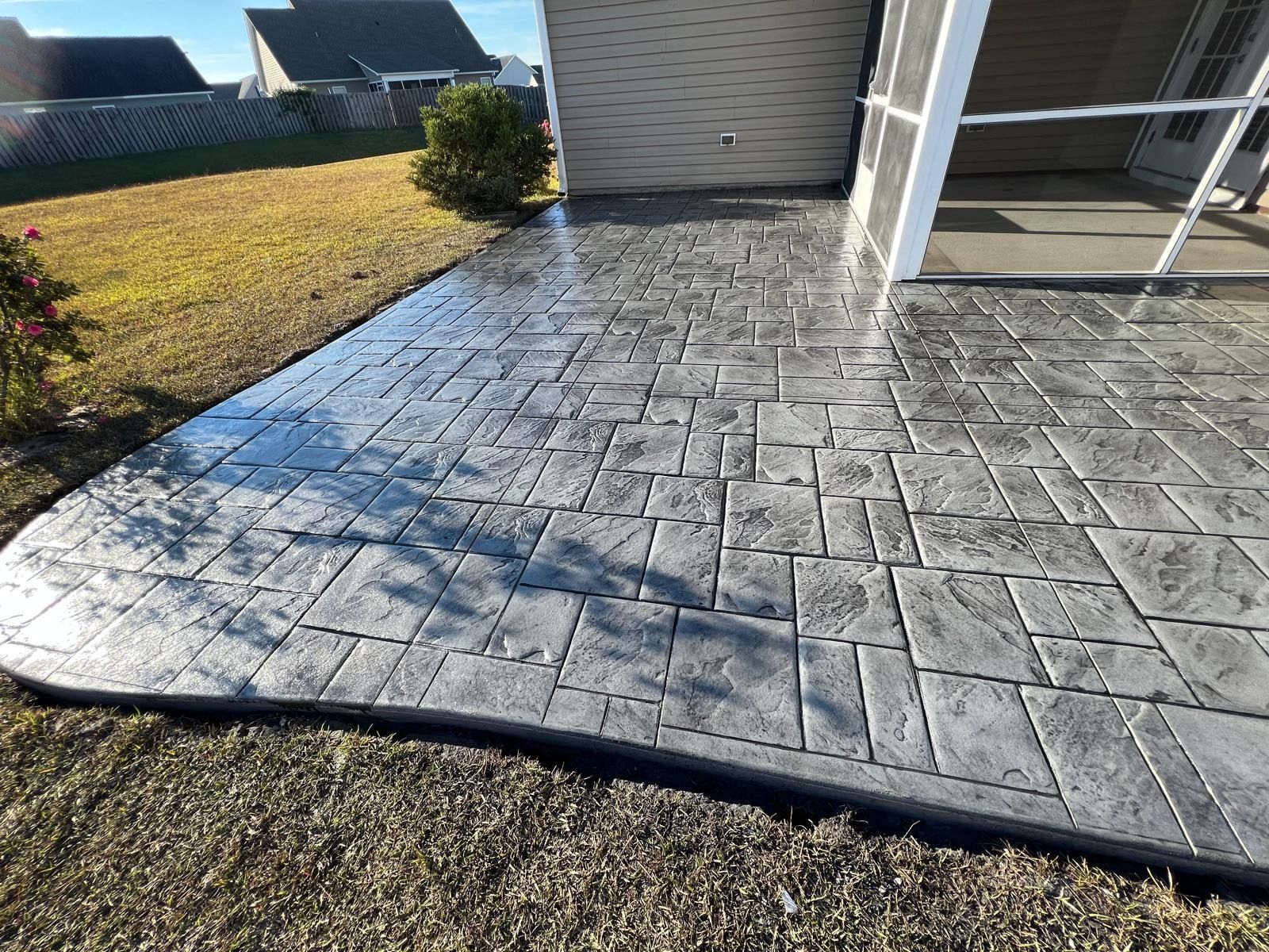 A concrete patio in front of a house with a screened in porch.