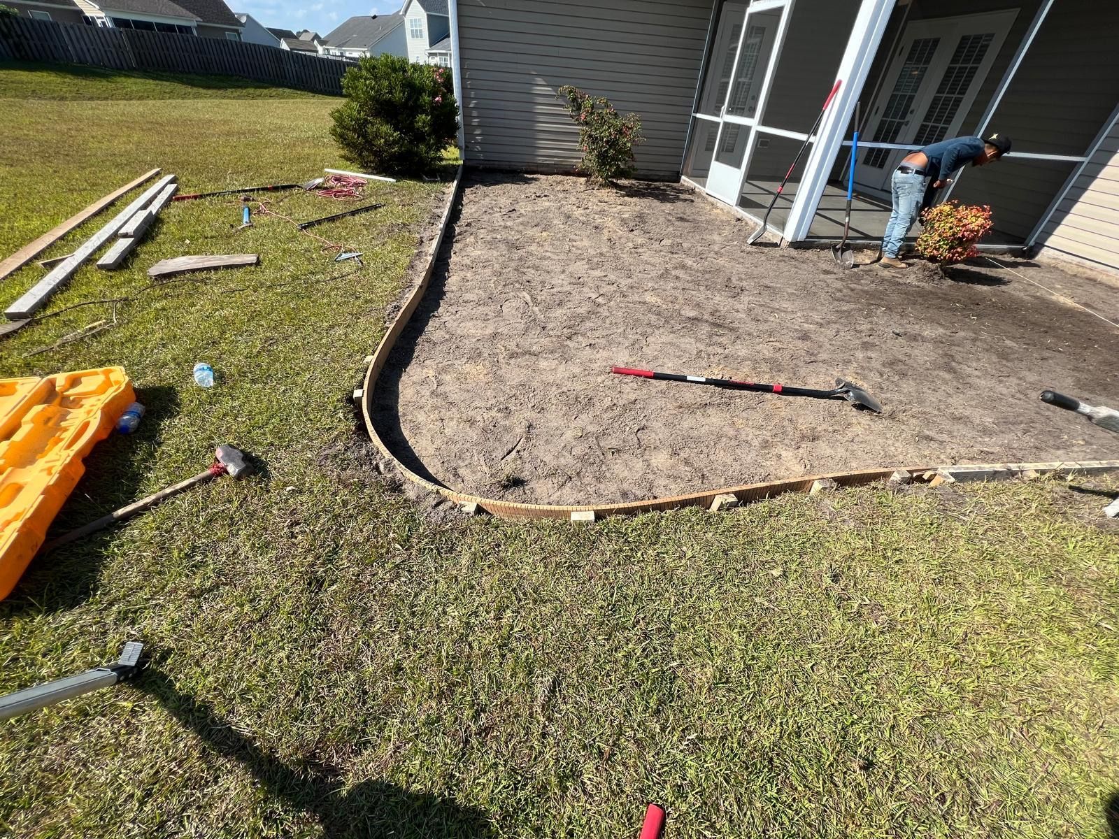 A man is working on a patio in the backyard of a house.