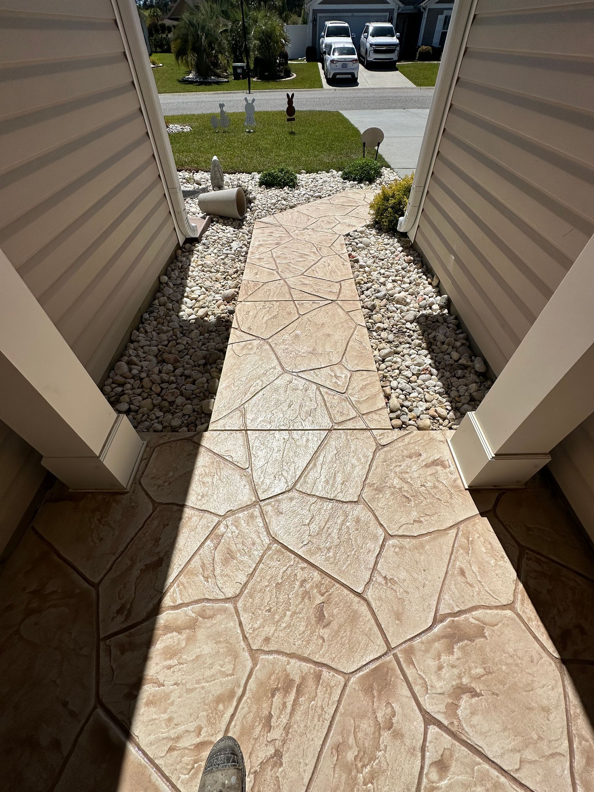 A stone walkway leading to a house with cars parked on the side of the road.