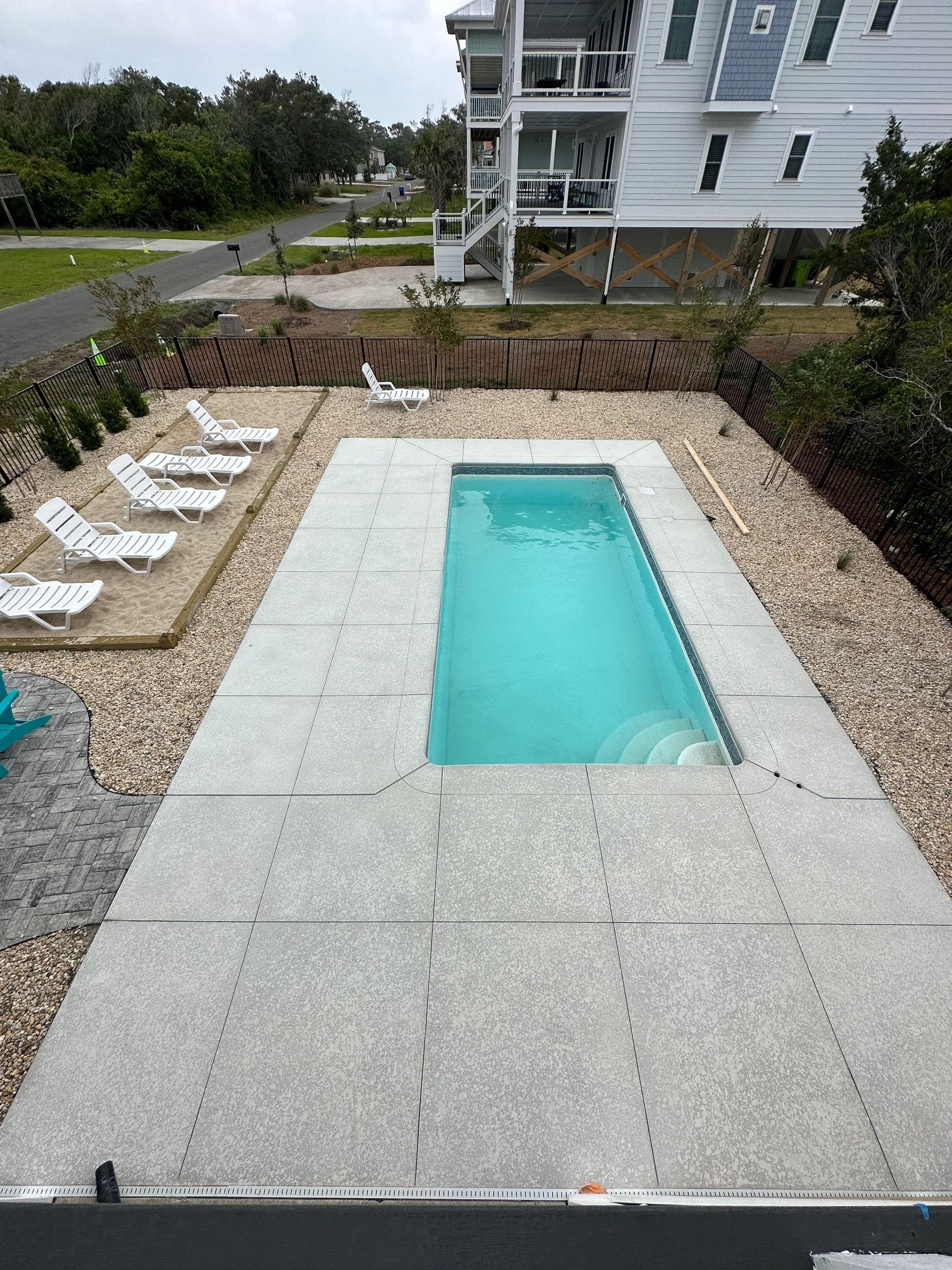 A large swimming pool is surrounded by chairs and gravel in front of a house.