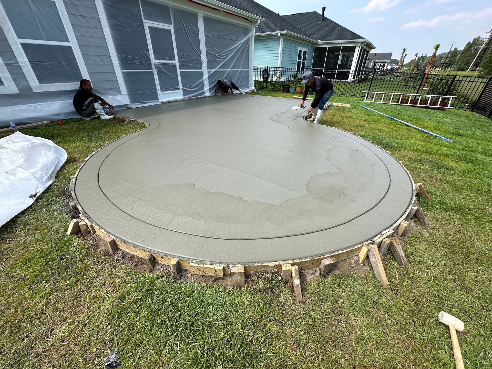 A man is laying concrete in a circle in a backyard.