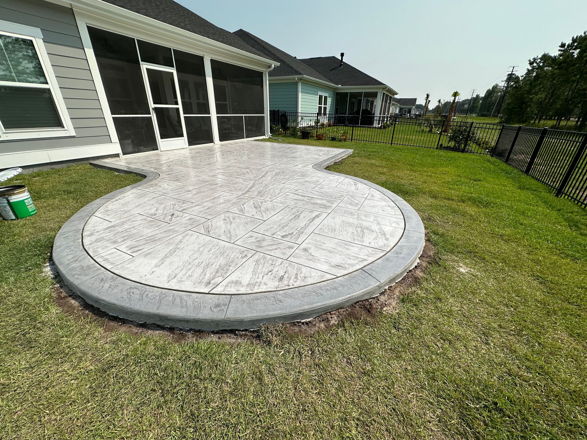 A concrete patio in the backyard of a house with a screened in porch.
