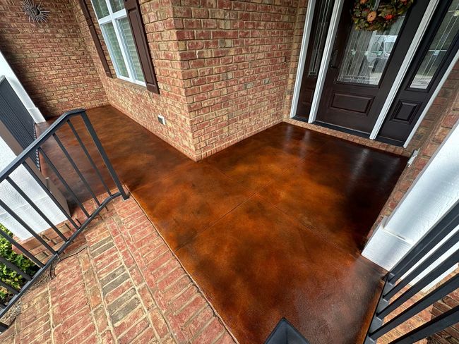 A stained concrete porch with a brick wall and a black door.