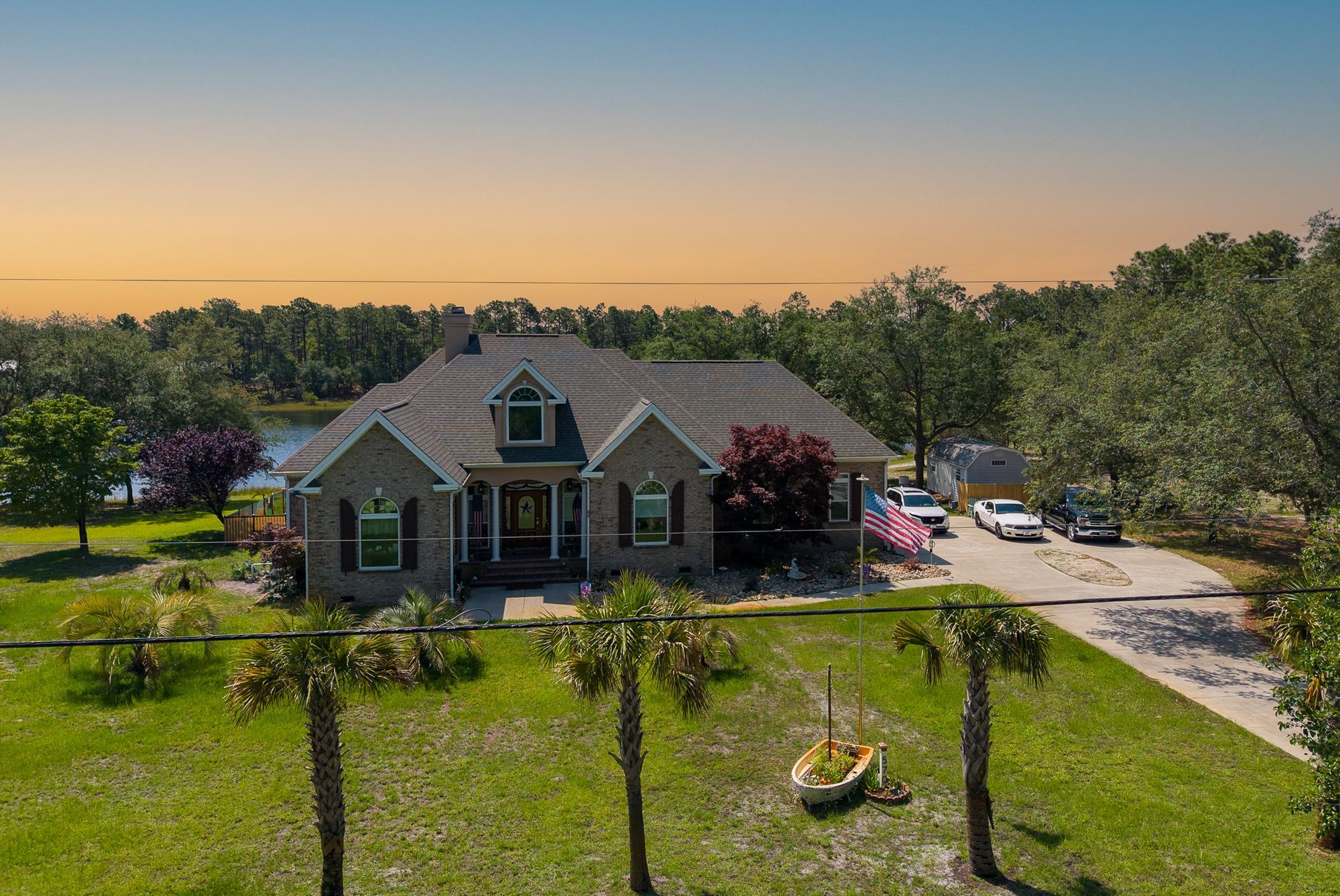 Brick house with a front porch and driveway at sunset, surrounded by a grassy yard and trees