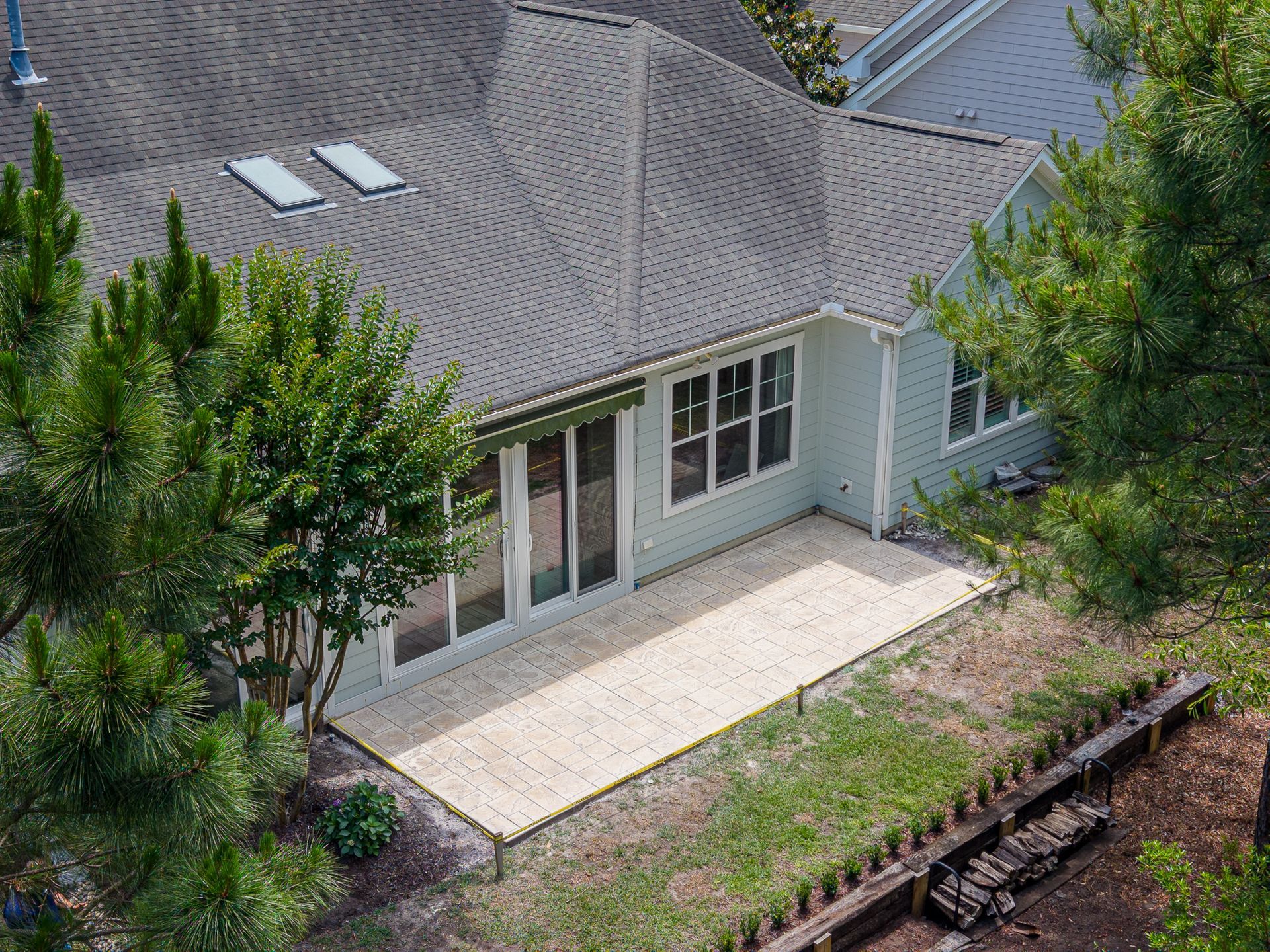 Aerial view of a house with a gray roof, white patio, and trees along a grassy yard.